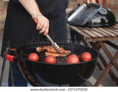 Man holding a beer grilling meat with tomatoes on a BBQ outdoors