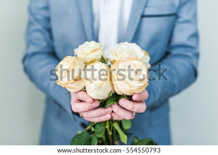 A man holding before him a bouquet of white roses. The guy covers his face with flowers. Valentine's day, international women's day, mother's day