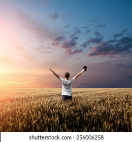 Man Holding Up Bible In A Wheat Field