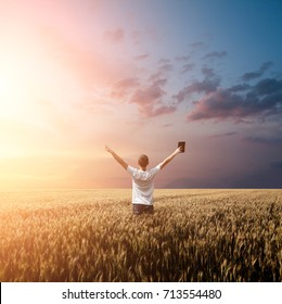 Man Holding Up Bible In A Wheat Field