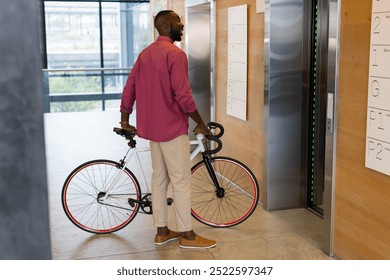 Man holding bicycle waiting for elevator in modern office building lobby. Urban, transportation, commuting, cyclist, business, corporate - Powered by Shutterstock