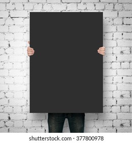 Man Holding Black Poster Mockup Over Brick Wall