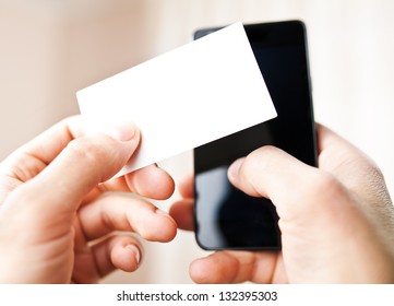 Man Holding Blank Business Card And Dialing Numbers On Mobile Phone