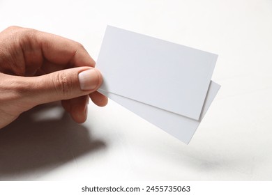 Man holding blank cards at white table, closeup. Mockup for design
