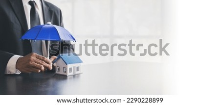 Man holding blue umbrella and white house. An insurance agent is holding a blue umbrella over a modern white house model. Property insurance concept. home and real estate insurance concepts.