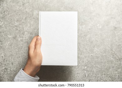 Man holding book with blank cover on grey background. Mock up for design