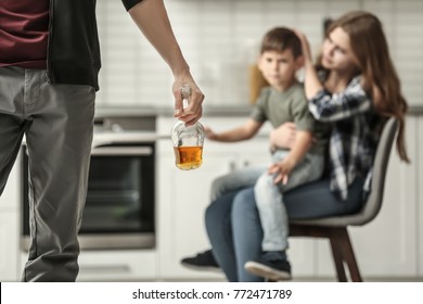 Man holding bottle of alcohol while wife hugging their son on background
