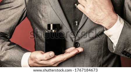 Man holding up bottle of perfume. Men perfume in the hand on suit background. Fragrance smell. Fashion cologne bottle. Man in formal suit, bottle of perfume, closeup. Men perfumes.