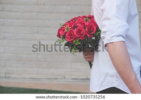 man holding bouquet of red roses behind his back. boyfriend surprise girlfriend with flower in valentine's day. celebrate anniversary, love & relationship concept