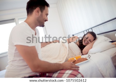 Man holding breakfast and tray to a happy girfriend in bed.