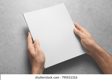 Man Holding Brochure With Blank Cover On Grey Background. Mock Up For Design
