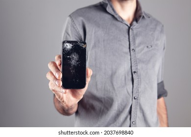 Man Holding Broken Phone On Gray Background