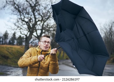 Man Holding Broken Umbrella In Strong Wind During Gloomy Rainy Day. Themes Weather And Meteorology. 