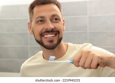 Man Holding Brush With Toothpaste In Bathroom