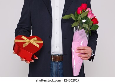 Man Holding A Bunch Of Flowers And A Heart Shaped Box Of Chocolates.