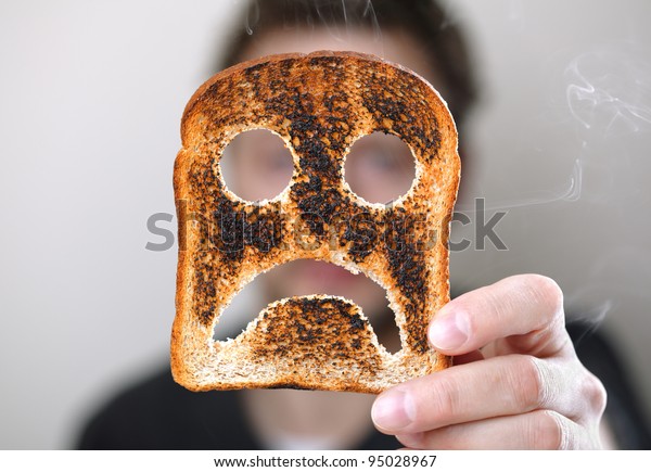 Man holding up a burnt slice of toast with an unhappy smiley concept for bad start to the day