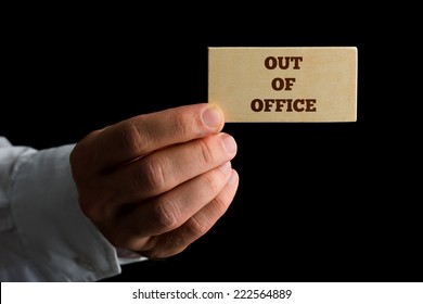 Man Holding A Business Card Reading - Out Of Office - Indicating That He And His Services Are Unavailable Due To Absence.