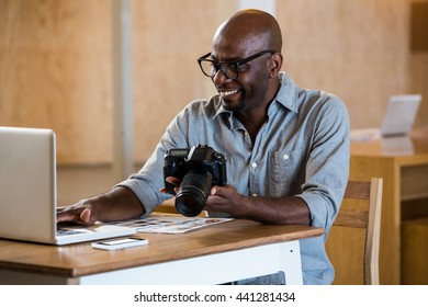 Man holding camera while using laptop in office