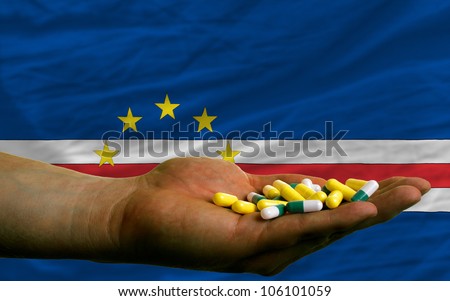 man holding capsules in front of complete wavy national flag of capeverde symbolizing health, medicine, cure, vitamins and healthy life