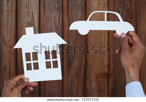 man\
holding a car and a house in paper against\
wood