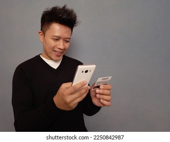 Man holding cell phone and credit card smiling.