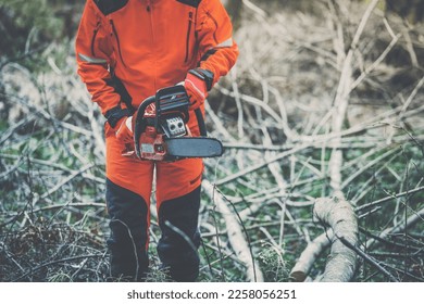 Hombre sosteniendo una motosierra y cortando árboles. El leñador en el trabajo lleva equipo de protección personal de color naranja. Jardinero trabajando al aire libre en el bosque. Profesionalidad de la seguridad ocupación concepto de trabajador forestal