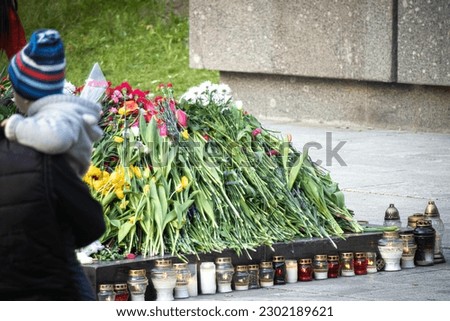 Man holding a child standing near snuffed out eternal fire surrounded with flowers during celebration of May 9 Victory Day in Vilnius, Lithuania Antakalnio cemetery