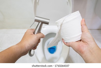 A man is holding and choosing between bidet shower and toilet paper