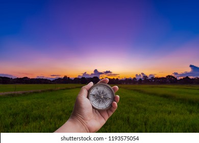 A Man Holding Compass On Hand At Field And Sunset For Navigation Guide.