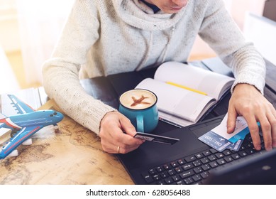 Man Holding A Credit Card And Buys Plane Tickets On The Internet Working On The Laptop. The Concept Of Travel And Transport, Buying And Booking