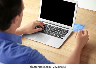Mann, der eine Kreditkarte besitzt, während er im Inneren einen Laptop verwendet