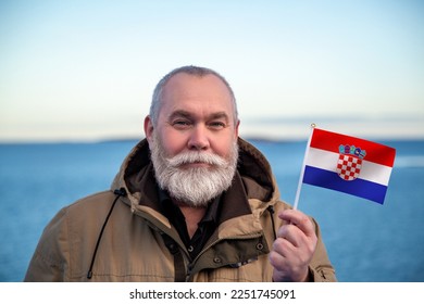 Man holding Croatia flag. 
Portrait of older man with a national Croatian flag. 
Visit Croatia. Older man 50 55 60 years old 
with gray beard outdoors travelling in winter. Travel to Croatia.