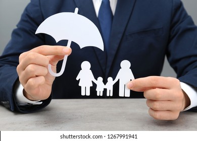 Man Holding Cutout Paper Family And Umbrella At Table, Closeup. Life Insurance Concept