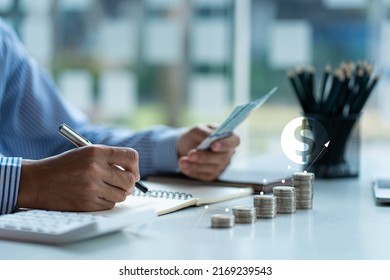 man holding dollar bill Keep a record of the amount he accumulates throughout the year with this pile of coins and piggy bank calculators for future business investments. - Shutterstock ID 2169239543