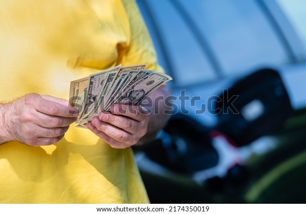 man holding dollar bills on background\
of car with open gas tank, close-up of\
hands