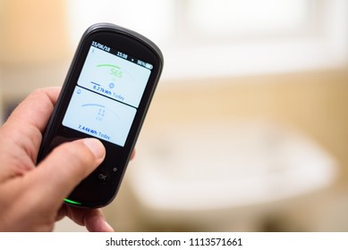 Man Holding A Domestic Energy Smart Meter Unit In A Bathroom, Displaying Energy Usage In Real Time