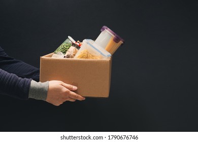 A man holding a donation box of different products on dark background - Powered by Shutterstock