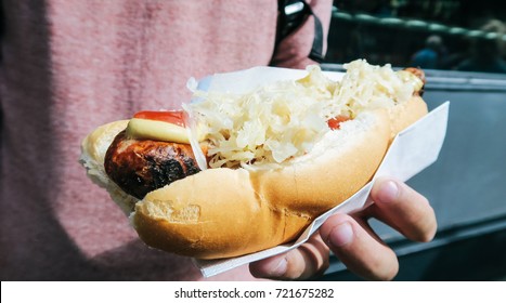 A man holding and eating a grilled sausage (bratwurst) with condiments are mustard, sauerkraut and sweet onions in bread, Borough Market, London, England, UK - Powered by Shutterstock