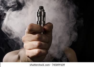 man holding electronic cigarette or vape device with smoke at the background.