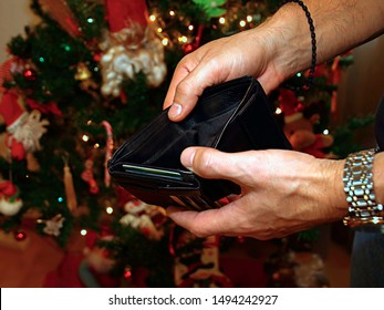 Man Holding An Empty Wallet In Front Of The Christmas Tree. No Money To Pay Christmas Shopping.