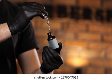 Man holding essential oil for beard in glass bottle on hand and dripping oil. man with black gloves in barber shop. copy space on bottle