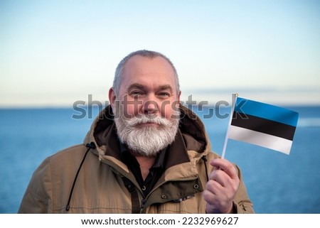 Man holding Estonia flag. 
Portrait of older man with a national Estonian flag. 
Visit Estonia concept. Older man 50 55 60 years old 
with gray beard outdoors travelling in winter. Travel to Tallinn
