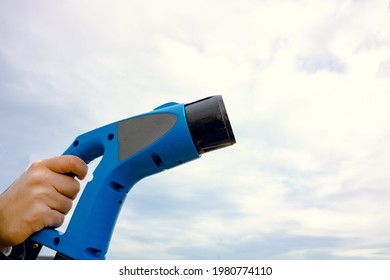 Man Holding A EV Charger Against The Cloudy Sky. Copy Space. EV Charger. Electric Vehicle Charging. Alternative Energy. Modern Technology. High Quality Photo