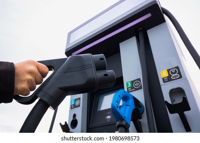 Man Holding A EV Charger. EV Charger Station On The Background. EV Charger Station Background. Alternative Energy. Electric Car Or Electric Vehicle. High Quality Photo