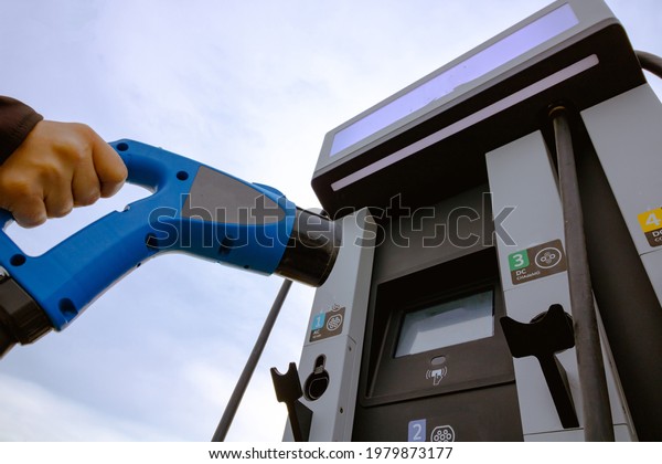 Man holding a EV\
charger. EV Charger station on the background. EV charger station\
background. Alternative energy. Electric car or electric vehicle.\
High quality photo