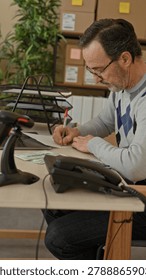 Man holding face with hands while counting money at parcel office desk with cardboard boxes and laptop in building; business worry.