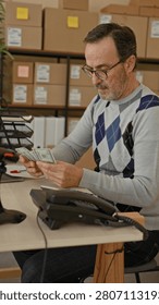 Man holding face with hands while counting money at parcel office desk with cardboard boxes and laptop in building; business worry.