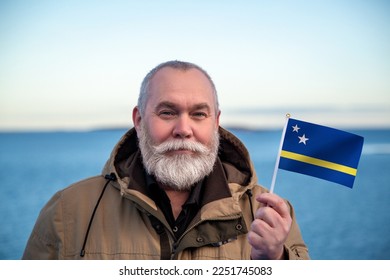 Man holding Curaçao flag. 
Portrait of older man with a national Curacao flag. 
Visit Curaçao concept. Older man 50 55 60 years old 
with gray beard outdoors travelling in winter.  - Shutterstock ID 2251745083