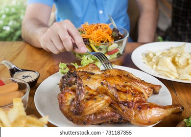 A Man Holding A Fork Is Eating A Grilled Chicken.