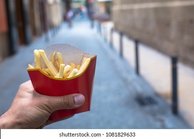 Man Holding French Fries In Hand In The Street. Small Pack Of Potato Fries